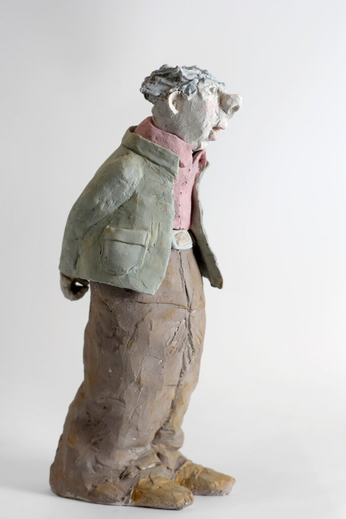 Sculpture figurative d'un personnage penché au visage naïf et rêveur en terre cuite, veste verte et chemise rose aux engobes
