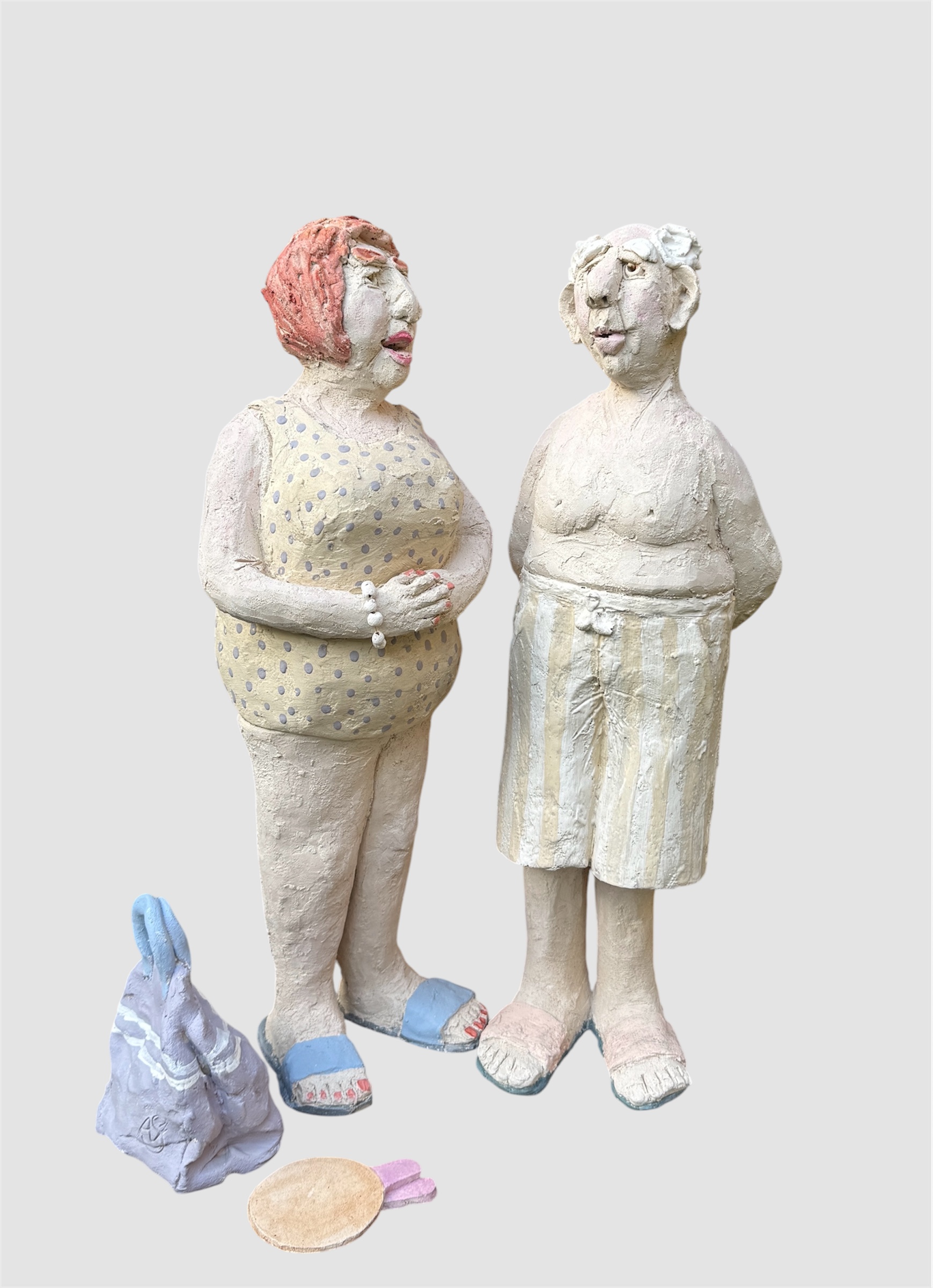 Sculpture figurative en terre cuite et engobes représentant un un couple vintage côte à côte avec sac de plage et raquettes au sol, homme en shprt rayé à l'expression douce et femme en maillot jaune à pois violet, cheveux colorés presque rouge et attitude affirmée